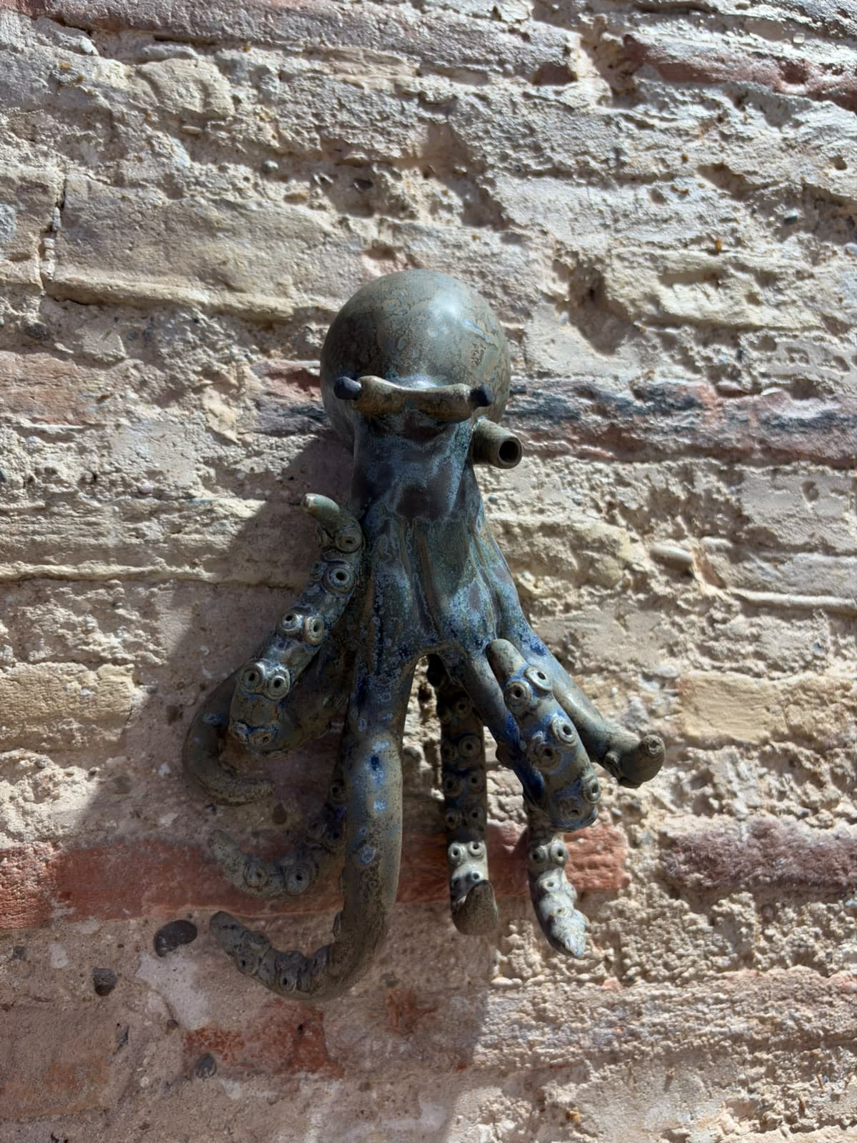Pulpo de cerámica azul y gris colgado en una pared de ladrillo